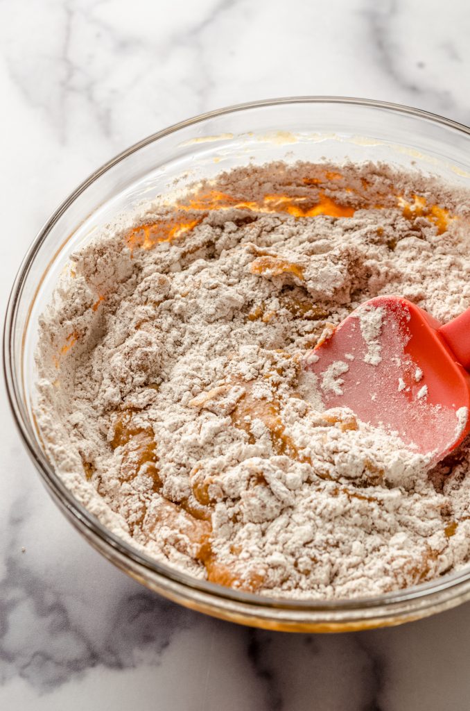 A spatula in a glass bowl mixing together the ingredients to make pumpkin donuts.