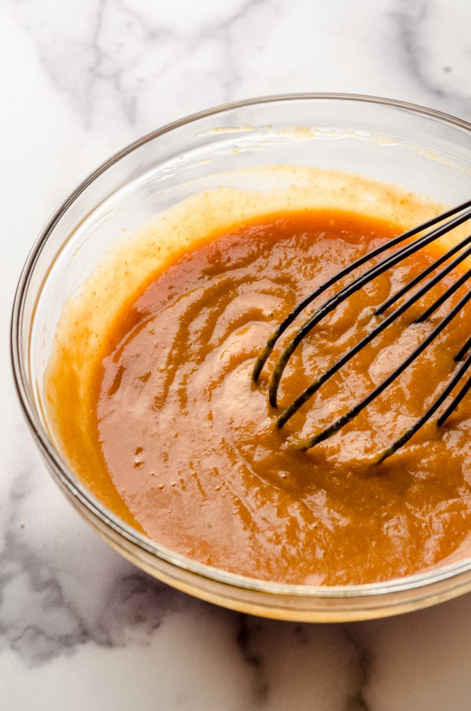 A whisk in a glass bowl mixing together the ingredients to make pumpkin donuts.