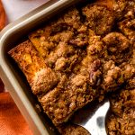 Aerial photo of someone lifting a slice of pumpkin French toast casserole out of a baking dish.