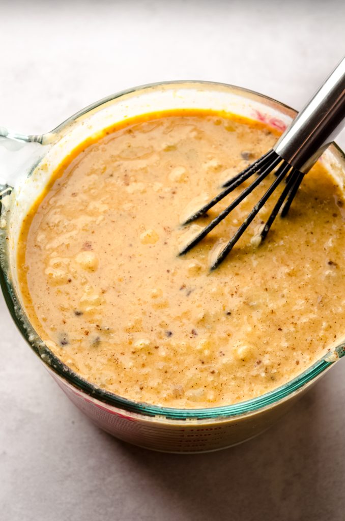 The custard part of a pumpkin French toast casserole in a large glass measuring cup with a whisk in it.