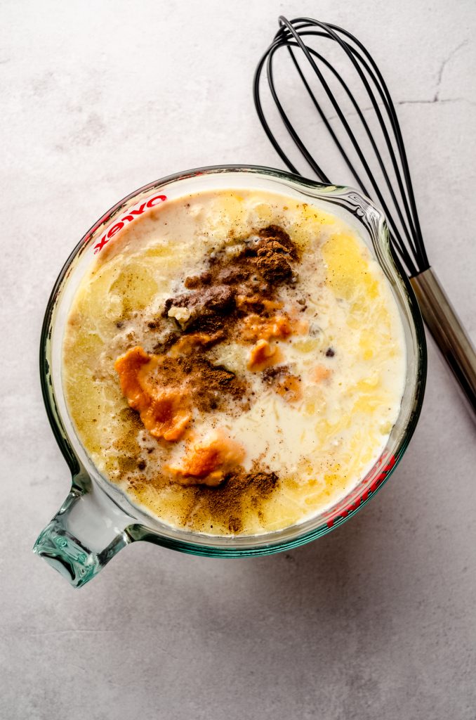 Aerial photo of the custard part of a pumpkin French toast casserole in a large glass measuring cup with a whisk off to the side.