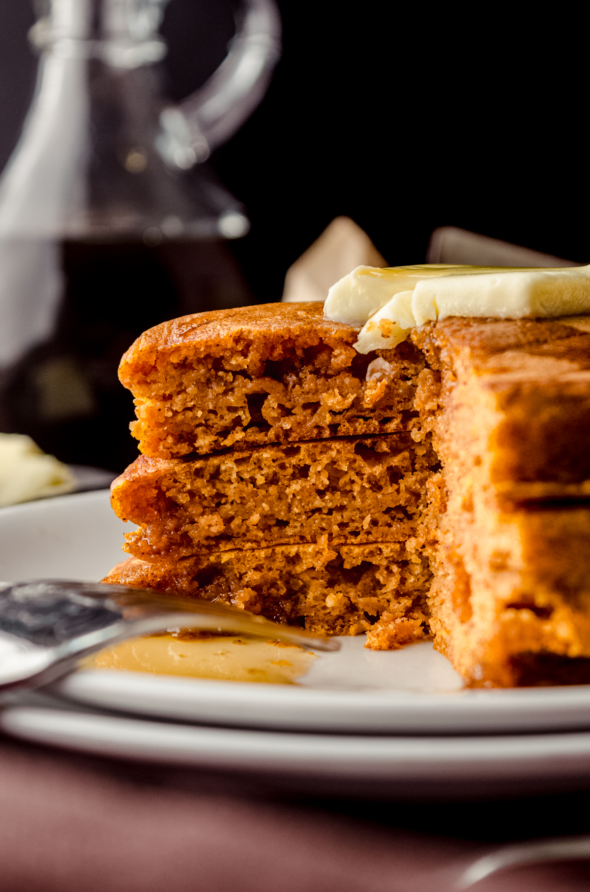 A stack of pumpkin pancakes with pats of butter and syrup on it that has been sliced so you can see the cross-section of pancakes.