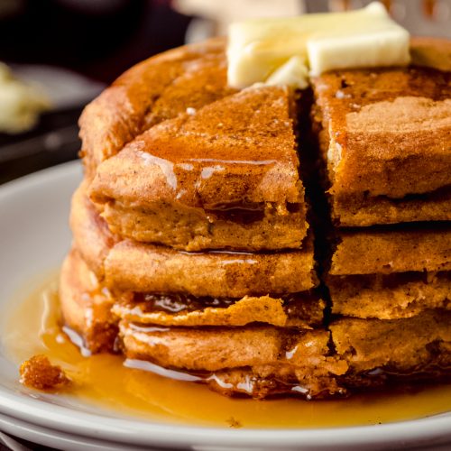 A stack of pumpkin pancakes with pats of butter and syrup on it that has been sliced into a triangle shaped stack of bites.