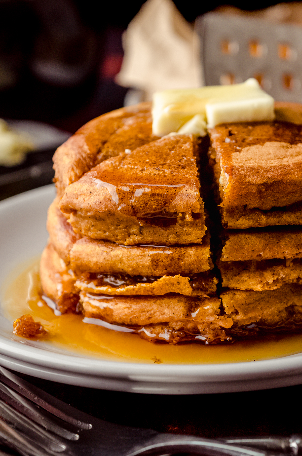 A stack of pumpkin pancakes with pats of butter and syrup on it that has been sliced into a triangle shaped stack of bites.