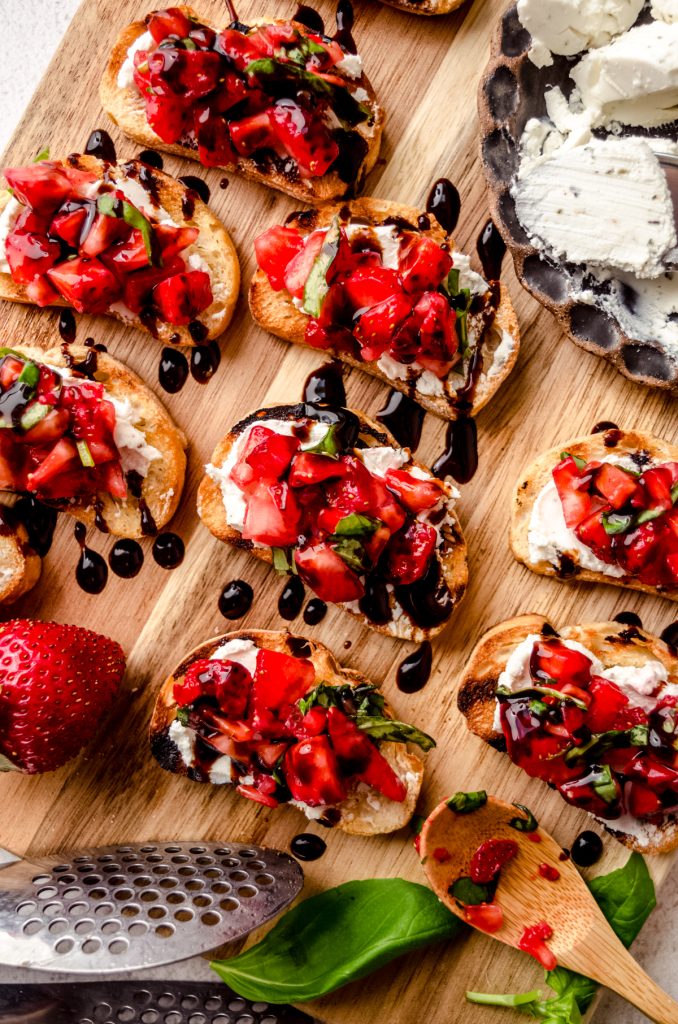 Aerial photo of strawberry goat cheese bruschetta pieces on a wooden cutting board.