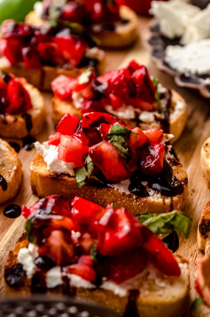 Strawberry goat cheese bruschetta pieces on a wooden cutting board.