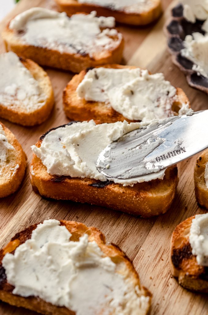 Someone is spreading French bread slices with goat cheese.