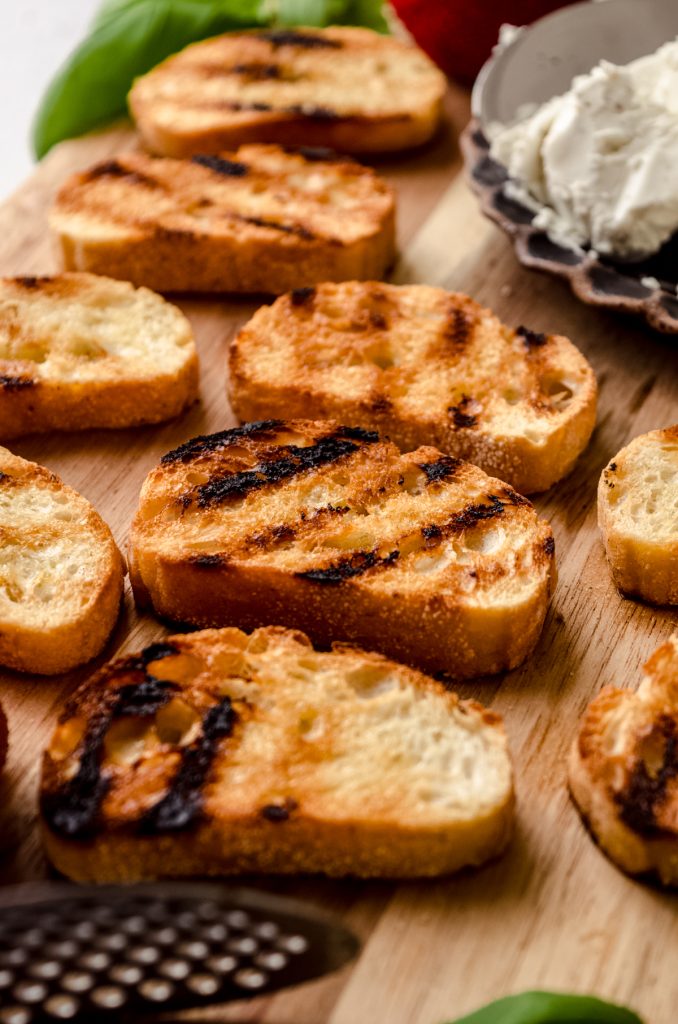 Grilled French bread slices on a wooden cutting board.