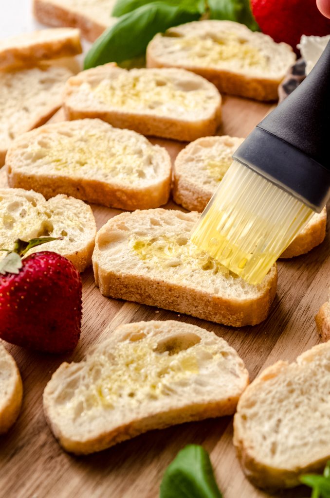 Someone is brushing French bread slices with olive oil before grilling.