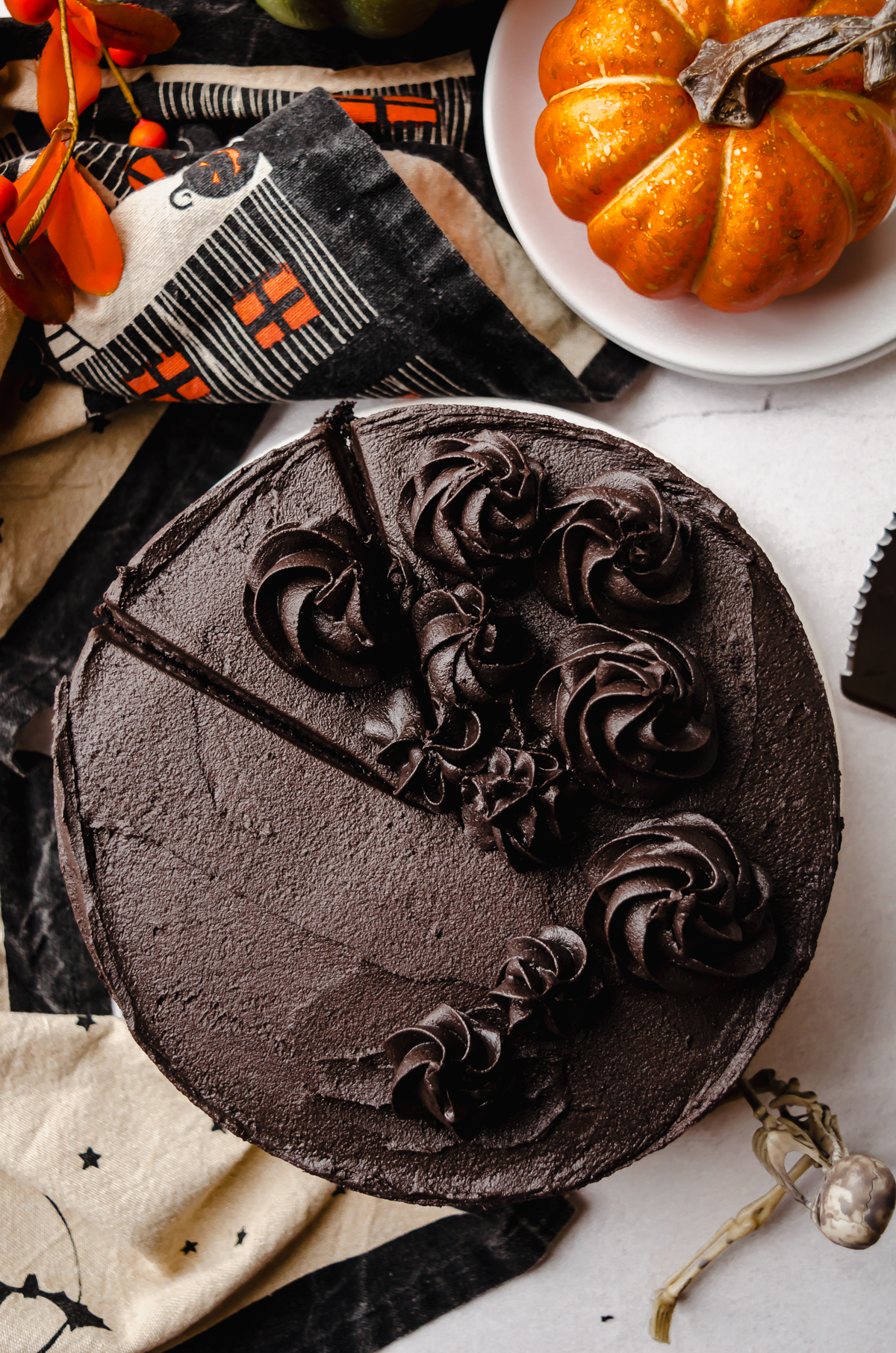 Aerial photo of a chocolate Halloween cake made with black cocoa powder on a plate and a slice has been cut but not yet removed.