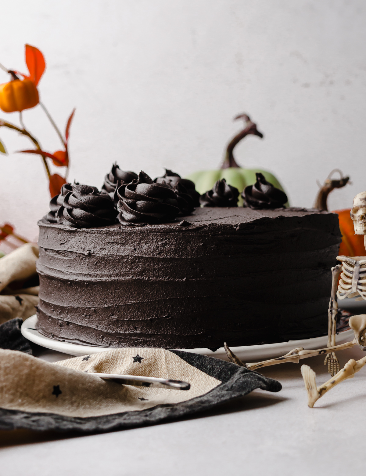 A black cocoa chocolate cake sitting on a plate with Halloween and autumn decor in the background.