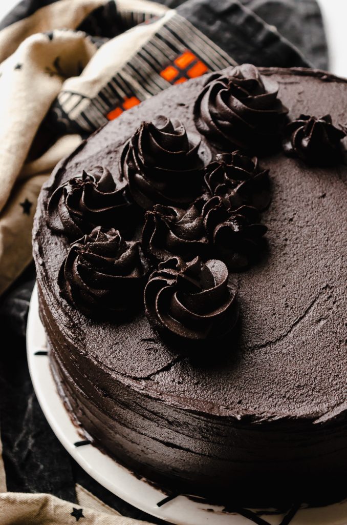 A black cocoa chocolate cake sitting on a plate with Halloween and autumn decor in the background.