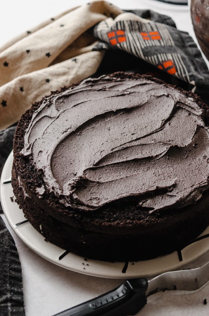 One layer of a chocolate Halloween cake on a plate and black cocoa chocolate frosting has been spread on the top of the layer.