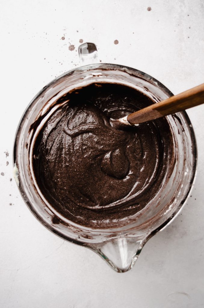 Aerial photo of batter for black cocoa chocolate cake in a glass bowl with a spatula.