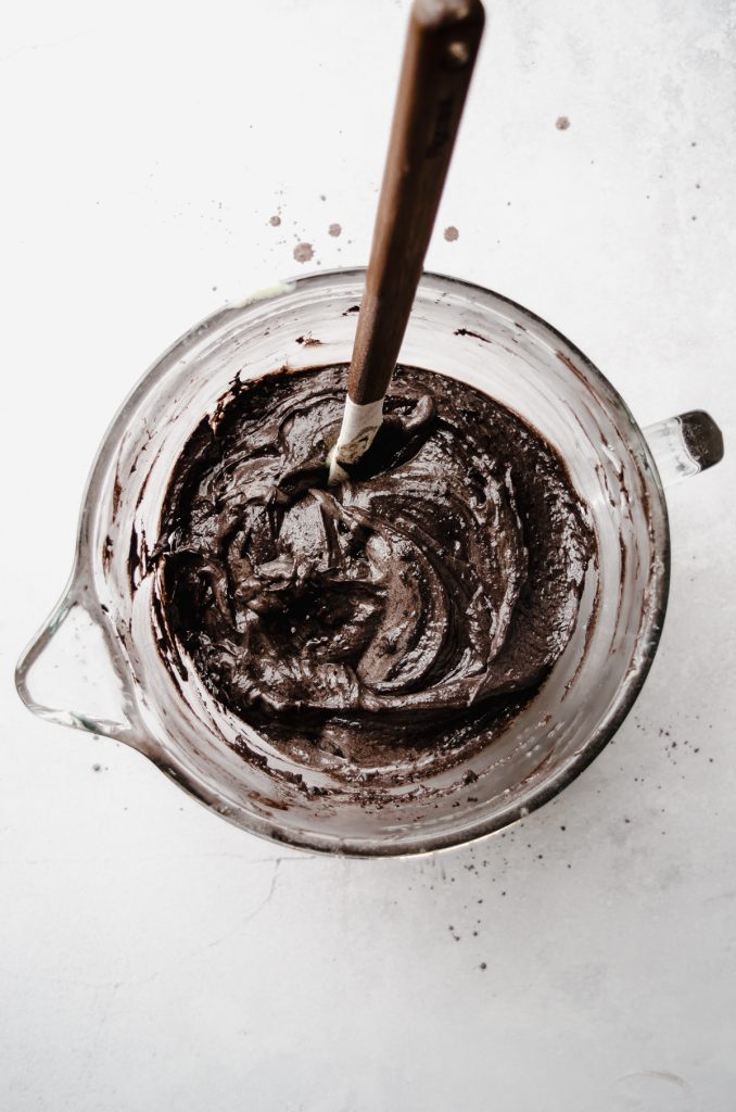 Aerial photo of batter for black cocoa chocolate cake in a glass bowl with a spatula.