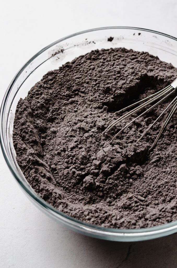 A bowl of dry ingredients to make black cocoa chocolate cake with a whisk in it.