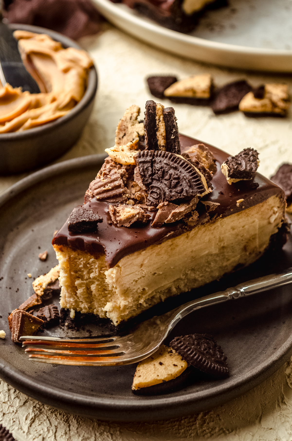 A photo of a slice of chocolate peanut butter cheesecake on a plate with a bite taken out of it.