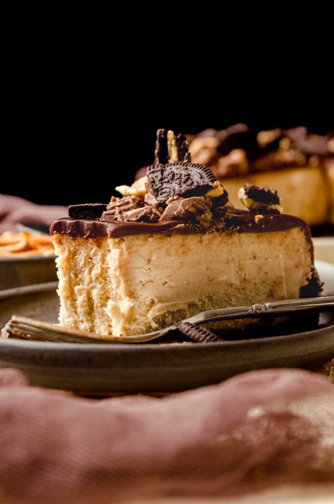 A photo of a slice of chocolate peanut butter cheesecake on a plate with a bite taken out of it.