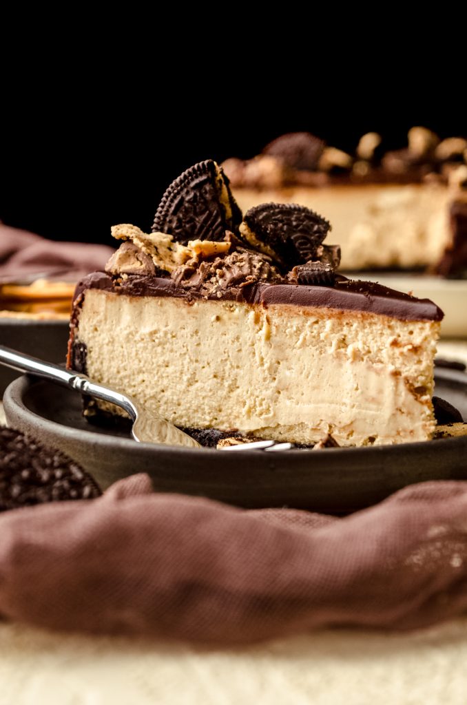 A photo of a slice of chocolate peanut butter cheesecake on a plate with a fork.