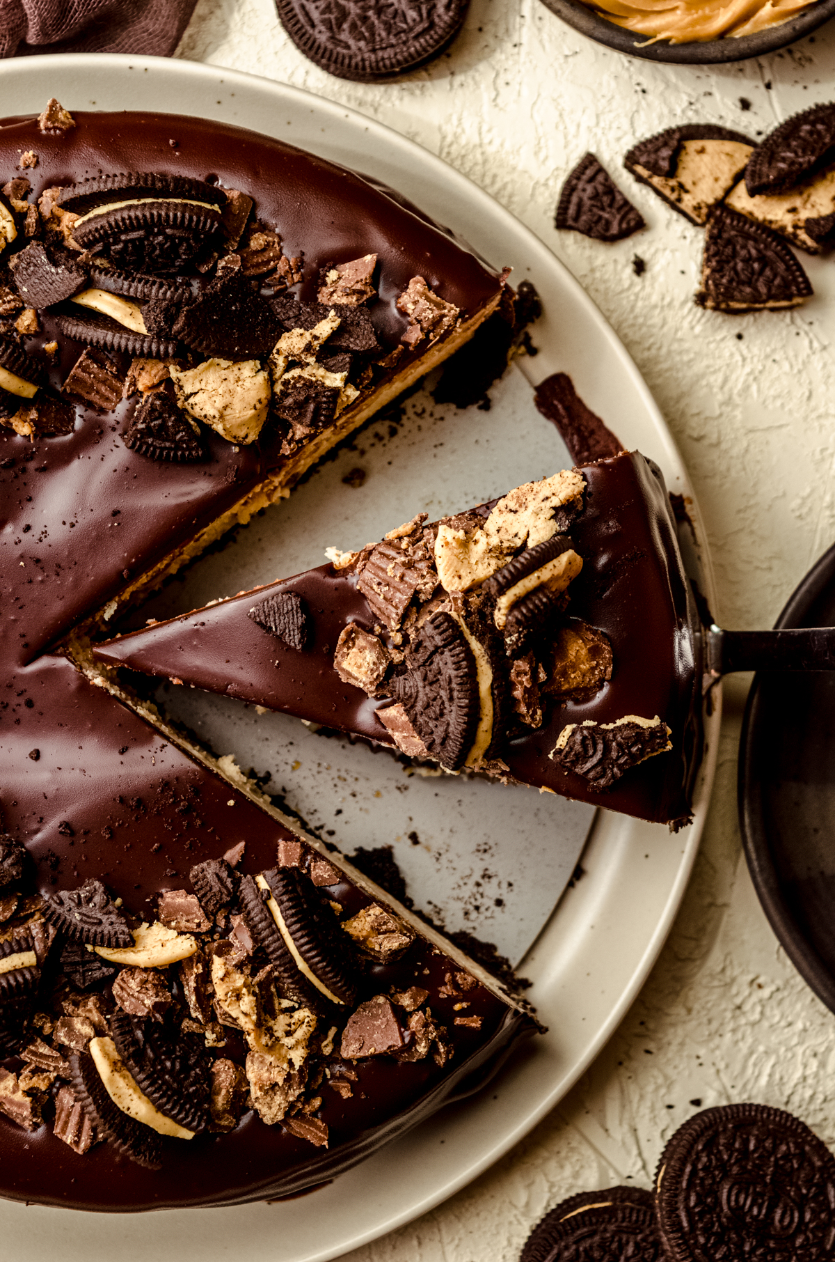 Aerial photo of someone pulling a slice of chocolate peanut butter cheesecake out of the whole cheesecake with a cake server.