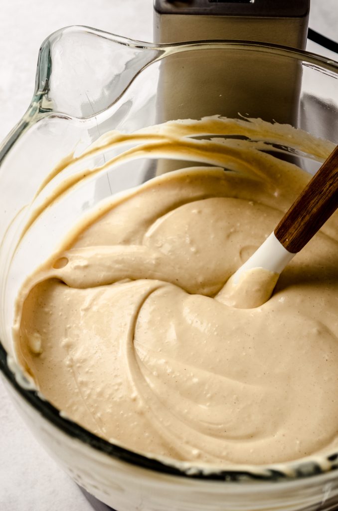 The batter for a peanut butter cheesecake in the bowl of a stand mixer with a spatula in it.