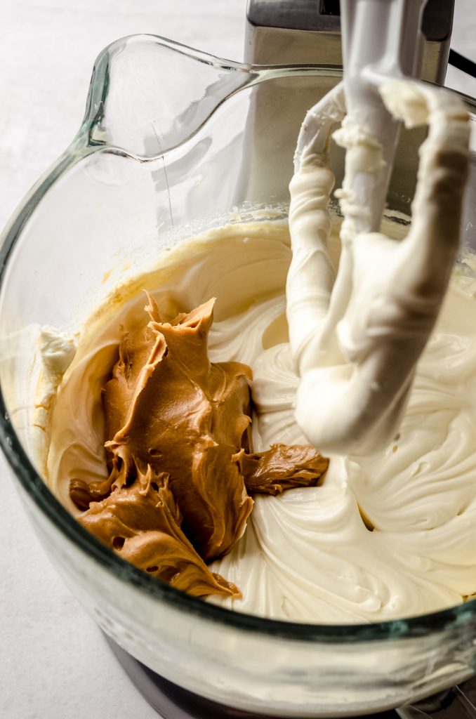 The batter for a peanut butter cheesecake in the bowl of a stand mixer with a spatula in it.