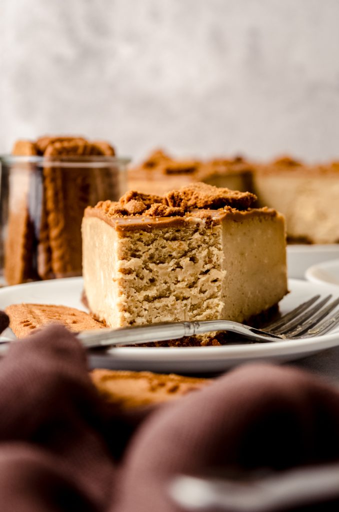 A slice of Biscoff cheesecake on a plate with a fork that has a bite taken out of it.