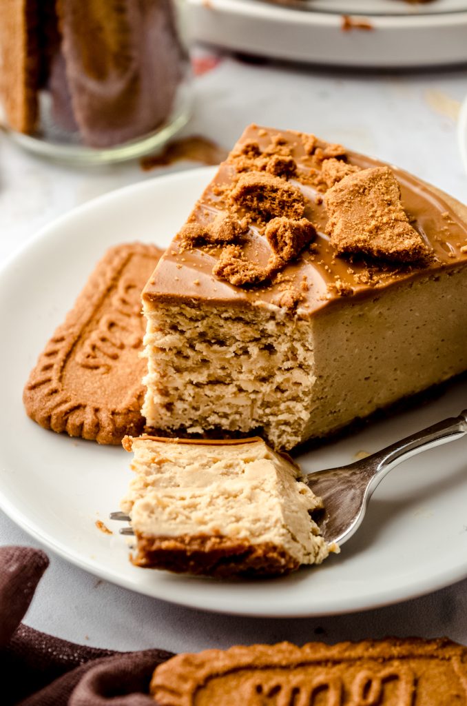 A slice of Biscoff cheesecake on a plate with a fork that has a bite taken out of it.