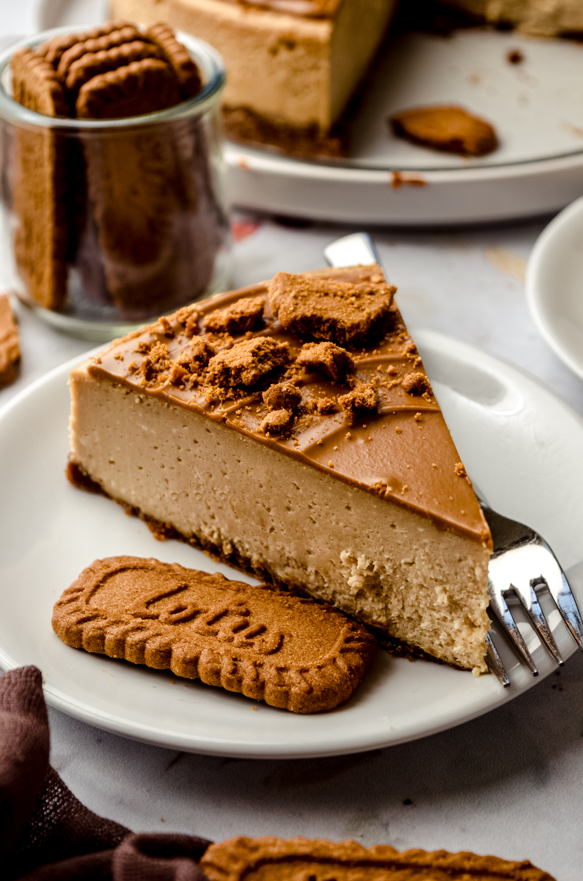 A slice of Biscoff cheesecake on a plate with a Biscoff cookie and a fork.