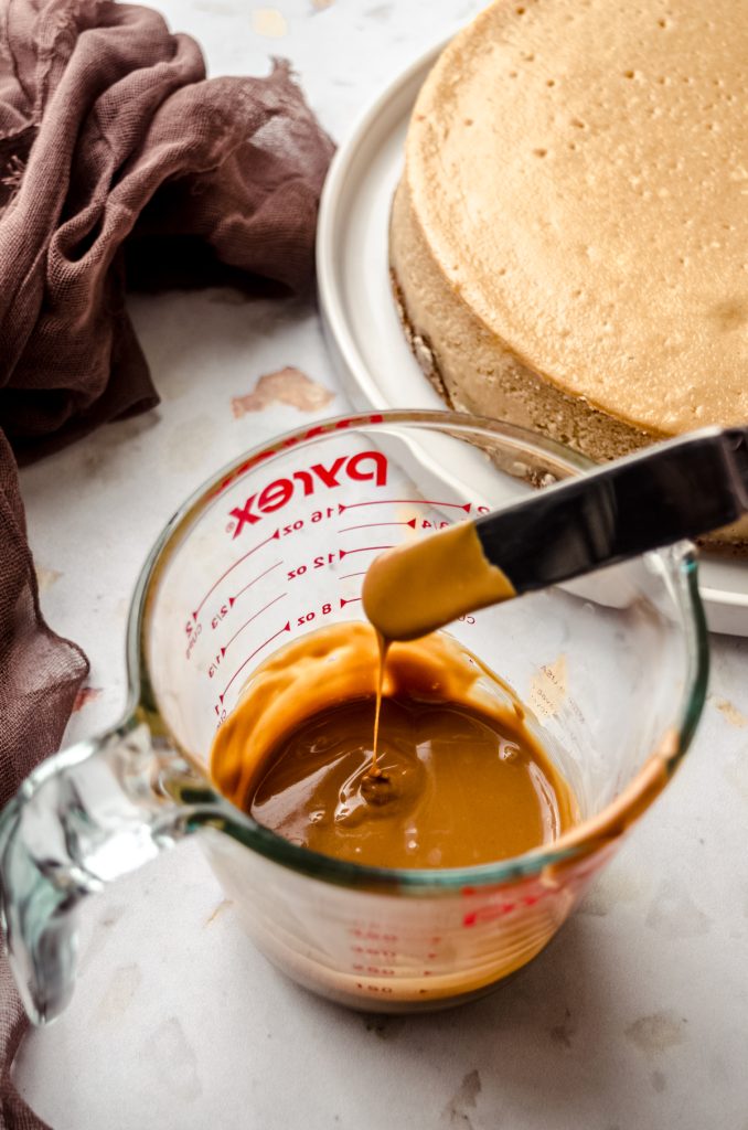 A glass measuring cup full of melted Biscoff and someone has put a spatula in it and is letting the excess drip off into the cup.