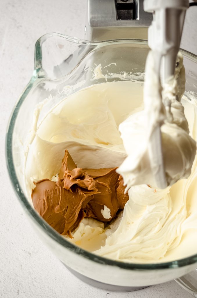 The bowl of a stand mixer with cheesecake filling ingredients in it mixed together and a dollop of Biscoff that is ready to be mixed in.