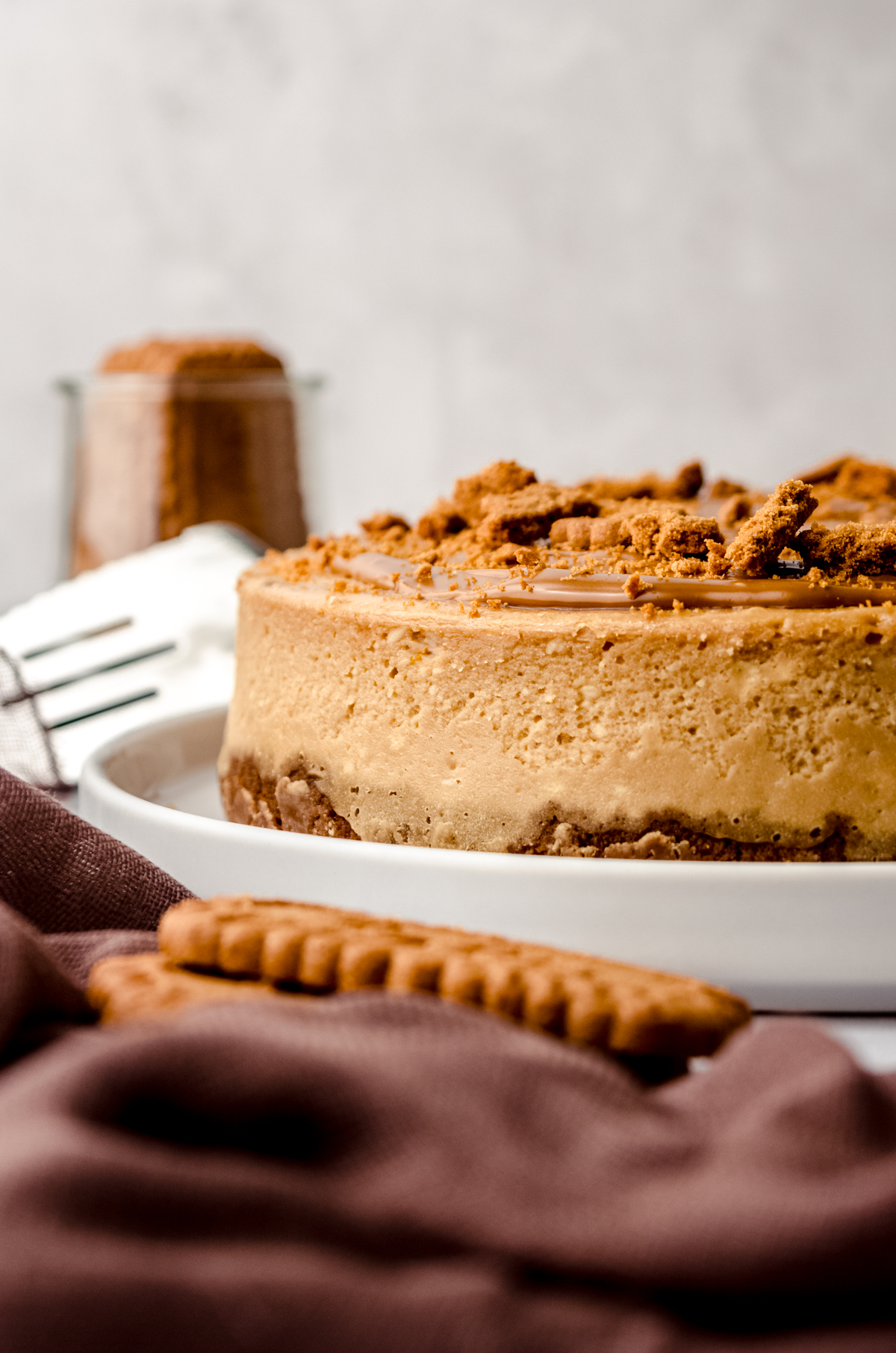 A Biscoff cheesecake on a plate with a spatula and cup of Biscoff cookies in the background.