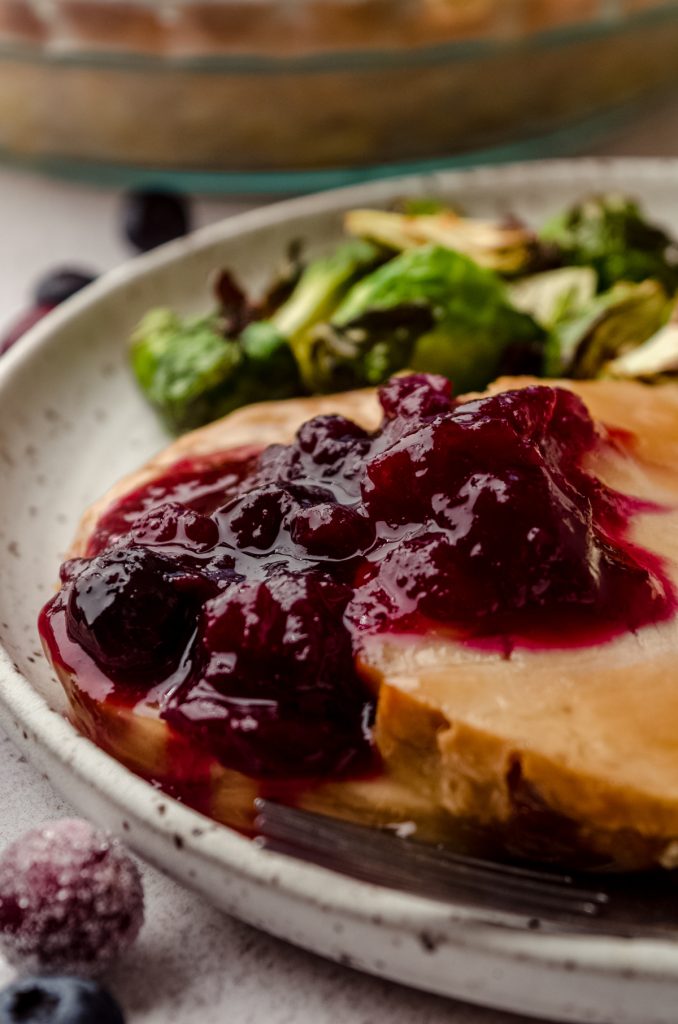 Blueberry cranberry sauce on slices of turkey on a plate with Brussels sprouts and a fork.