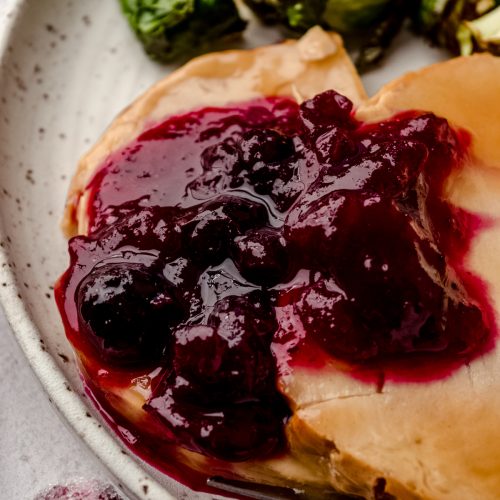 Blueberry cranberry sauce on slices of turkey on a plate with Brussels sprouts and a fork.