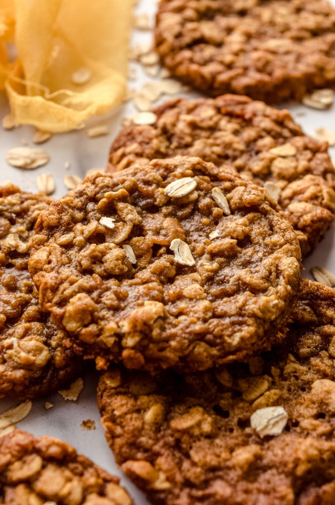 Chewy oatmeal cookies on a surface with oats scattered around.