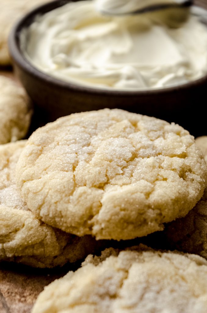 Cream cheese sugar cookies on a surface with a bowl of cream cheese in the background.