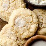 Aerial photo of cream cheese sugar cookies on a surface with a small bowl of sugar and a bowl of cream cheese.