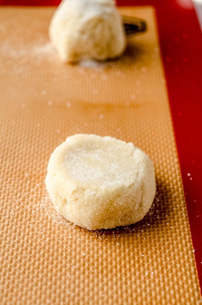 A cookie dough ball that has been flattened on a baking sheet.