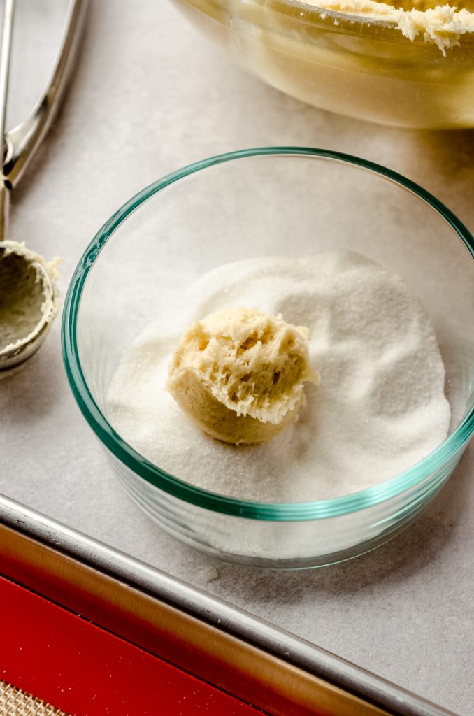 A ball of cream cheese sugar cookie dough in a bowl of granulated sugar.