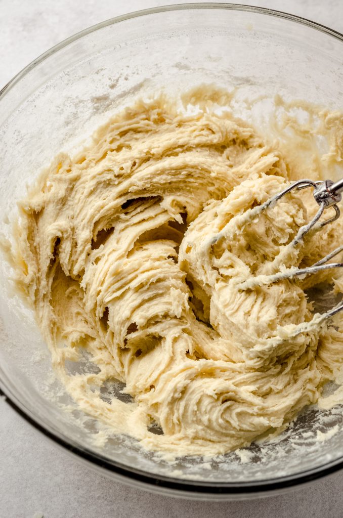 A bowl of cream cheese sugar cookie dough with electric beaters.