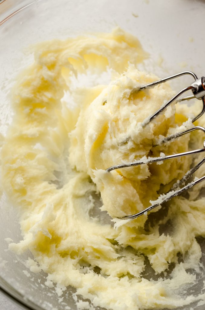 A bowl of cream cheese sugar cookie dough with electric beaters.