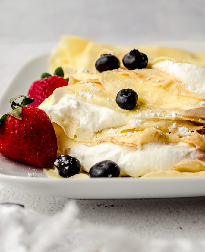 A photo of crepes on a plate with fresh whipped cream, blueberries, and strawberries on them.