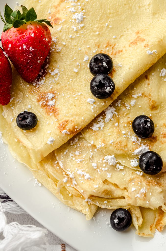 A photo of crepes on a plate with powdered sugar, blueberries, and strawberries on them.