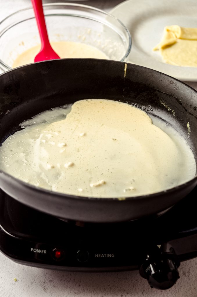 A photo of a pan being swirled by someone to make crepes.