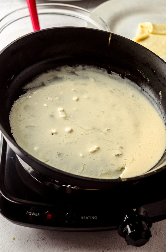 A photo of a pan being swirled by someone to make crepes.