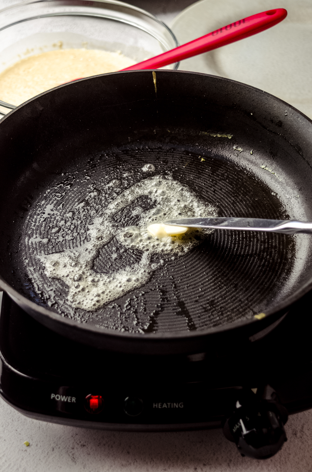 Someone is using a butter knife to butter a skillet to make crepes.