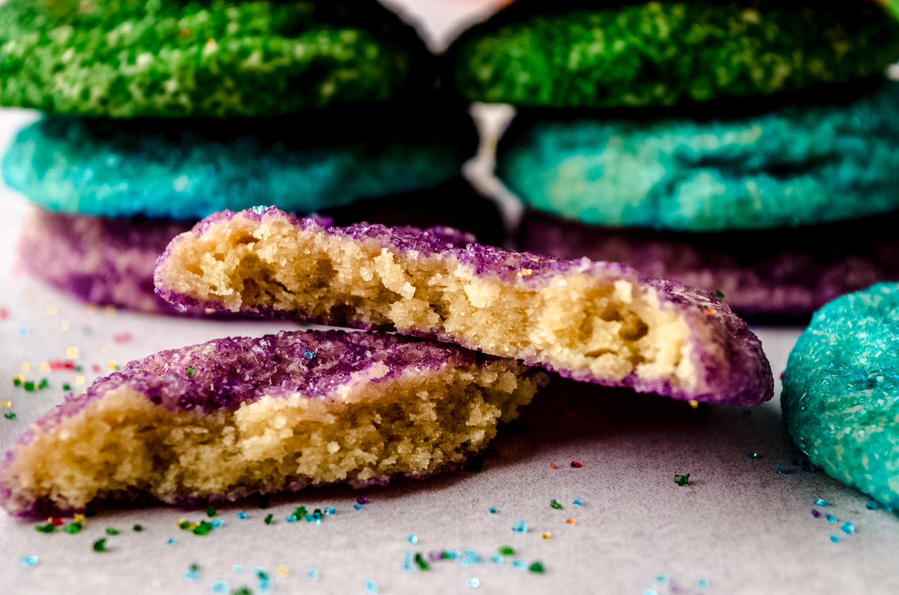 A purple sugar cookie split in half to see the cross-section on a surface and you can see green and blue ones in the background.