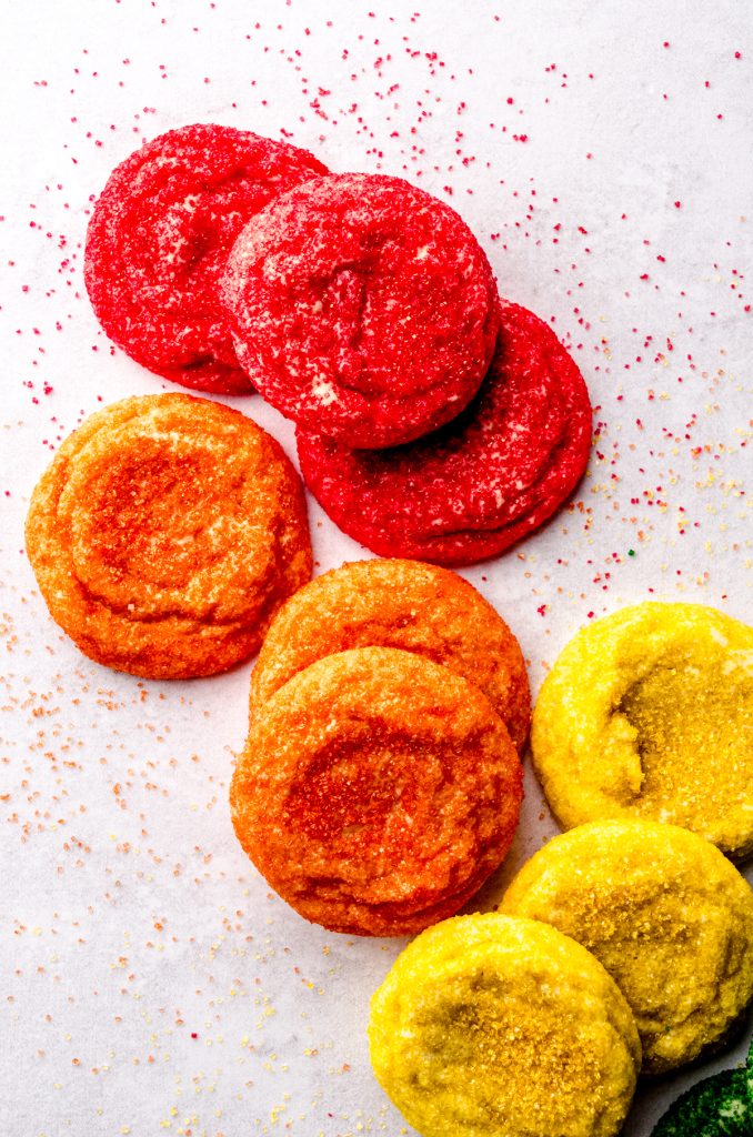 An aerial photo of sugar cookies coated in red, orange, and yellow, arranged on a surface in color order.