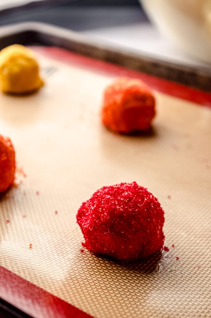 Red, orange, and yellow sugar cookie dough balls on a baking sheet.