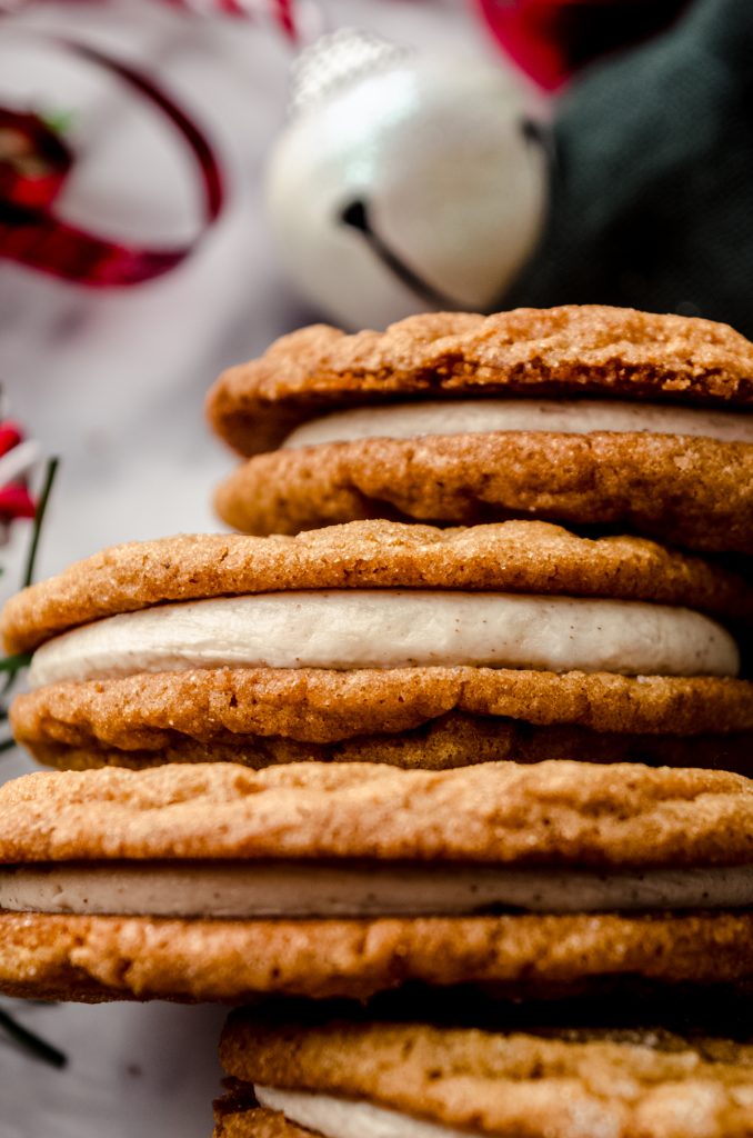 Gingerbread sandwich cookies on a surface and you can see Christmas bells and other decor in the background.